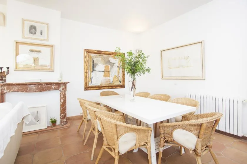 A bright dining area with a white table, wicker seating, and framed artwork.