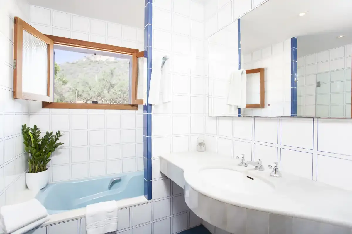 A tiled bathroom with a bathtub, sink, and open window.