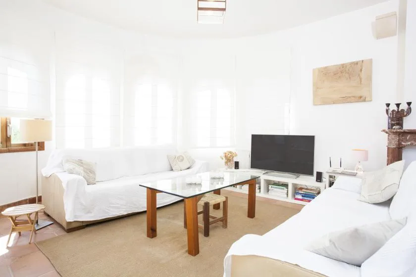 A bright living room with white seating and a glass coffee table.