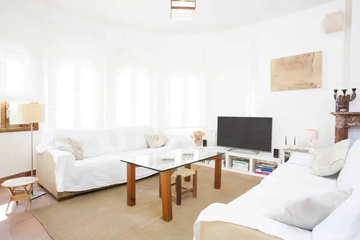 A bright living room with white seating and a glass coffee table.