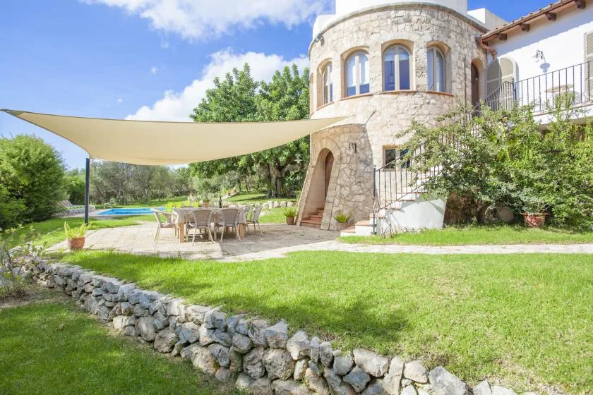 A stone house opens onto a lawn, with shaded outdoor seating and a pool nearby.