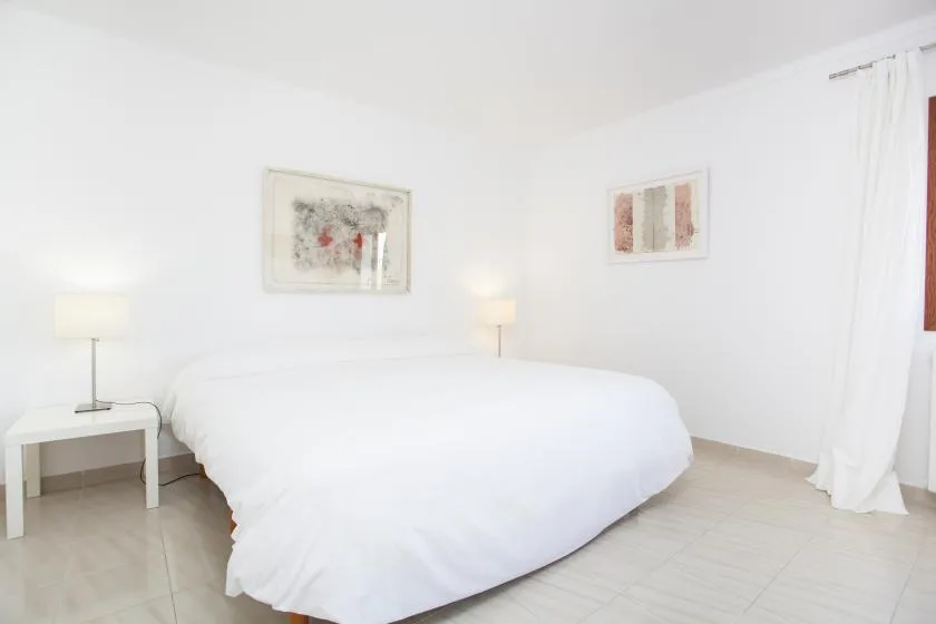 A bright bedroom with a white bed, bedside table, and framed artwork.