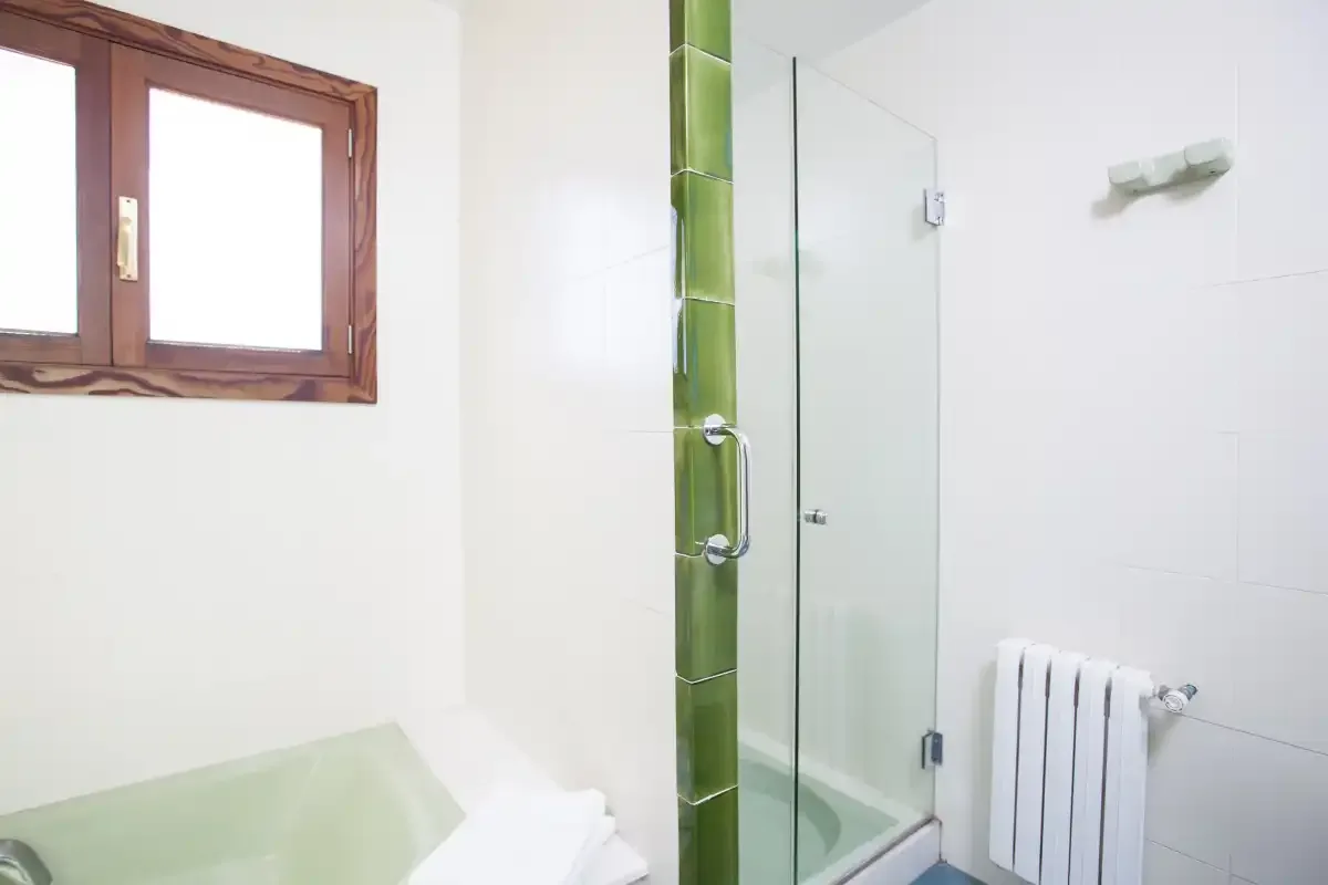 A bright bathroom with a glass shower beside a small window.