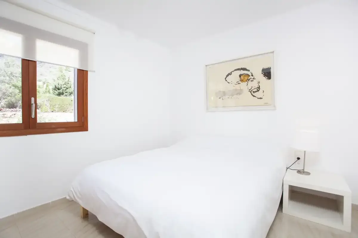A bright bedroom with a white bed, a window, and framed artwork.