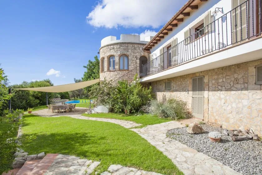 A stone house borders a green garden with a shaded outdoor seating area.