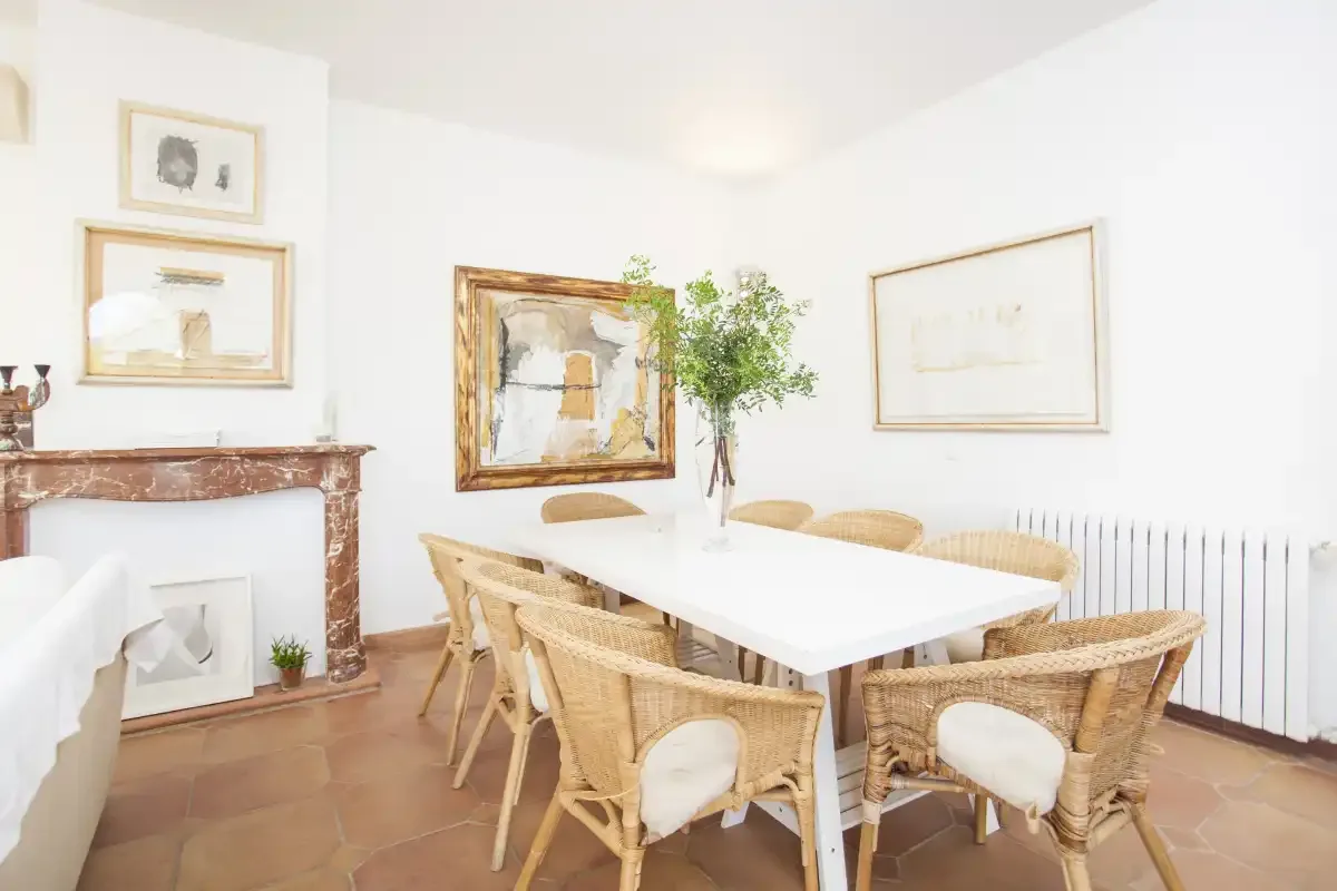 A bright dining room with a long table and woven seating.