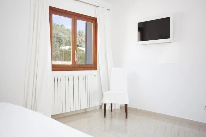 A bright room with a window, a chair, and a wall-mounted television.