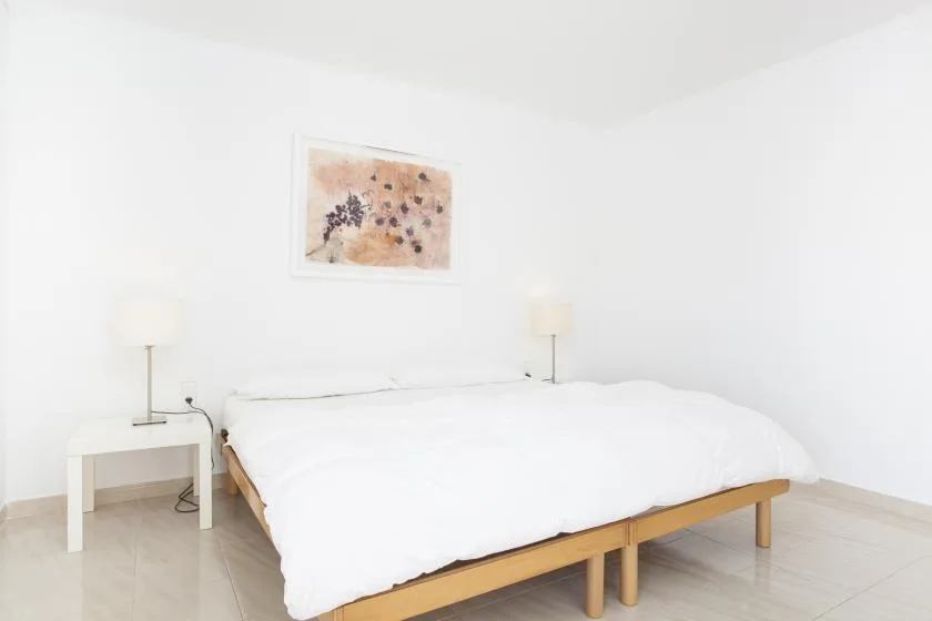 A bright bedroom with a white bed and framed artwork above it.