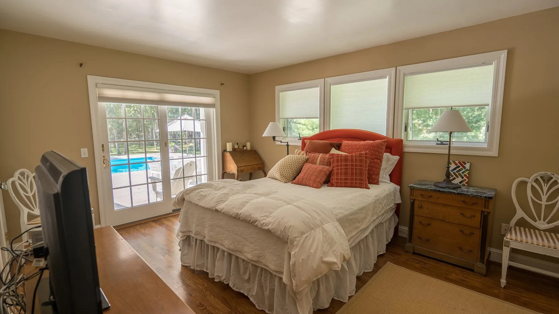 Un dormitorio con una cama, muebles junto a ella y ventanas con vista a una piscina exterior.