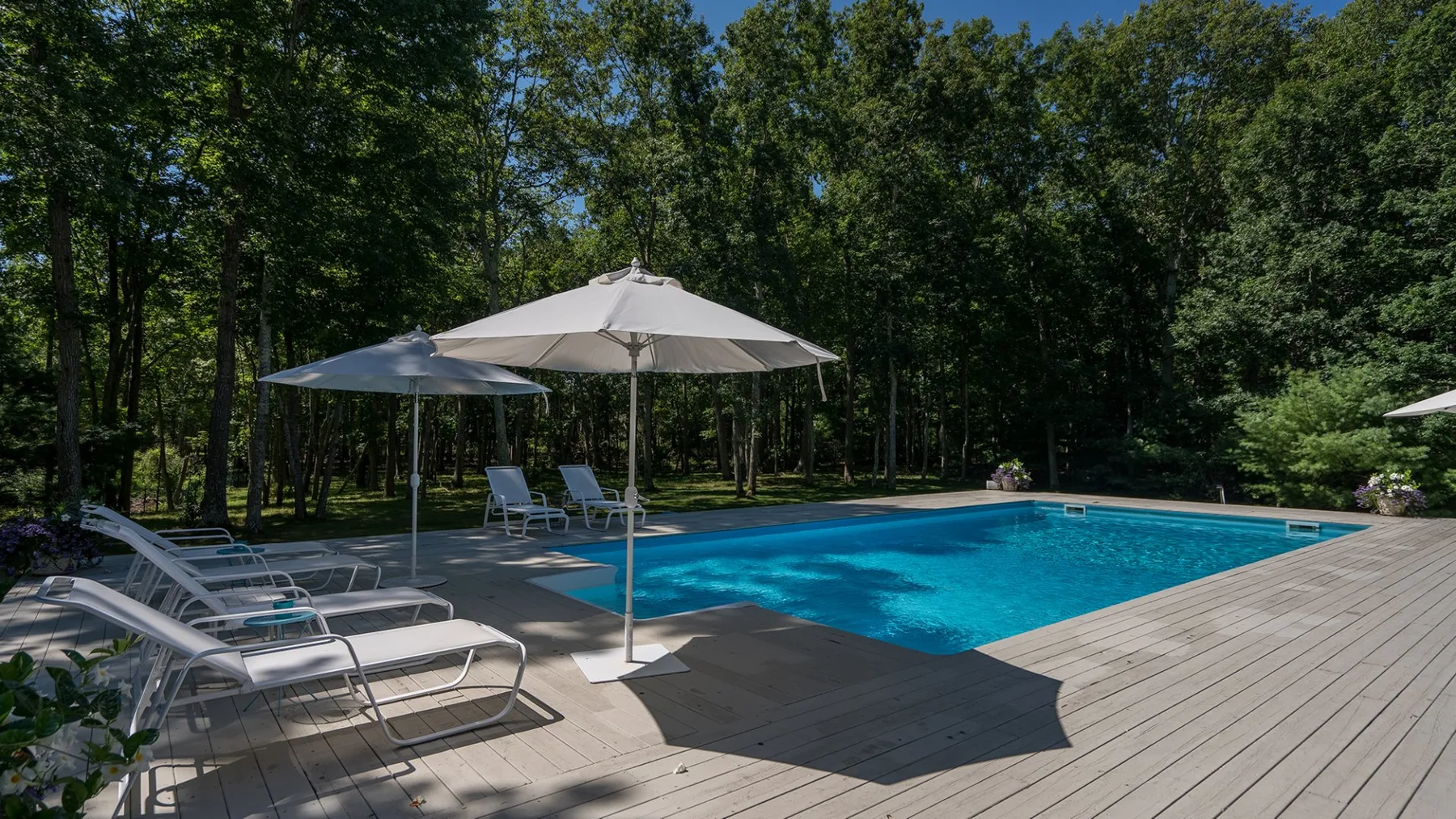 An outdoor swimming pool beside a wooden deck with loungers and umbrellas.