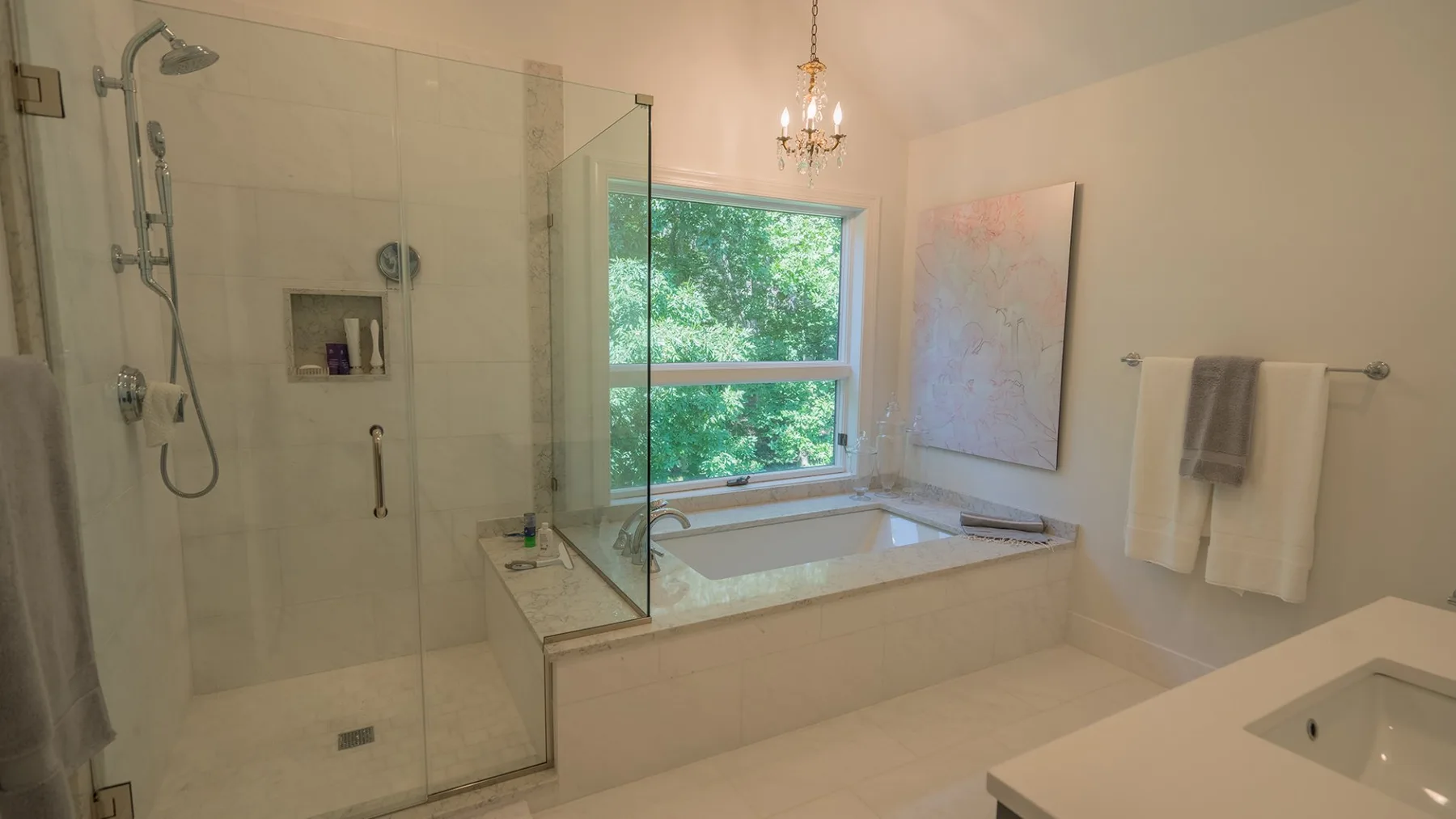 Un baño luminoso cuenta con una ducha de vidrio, una bañera y una ventana amplia.