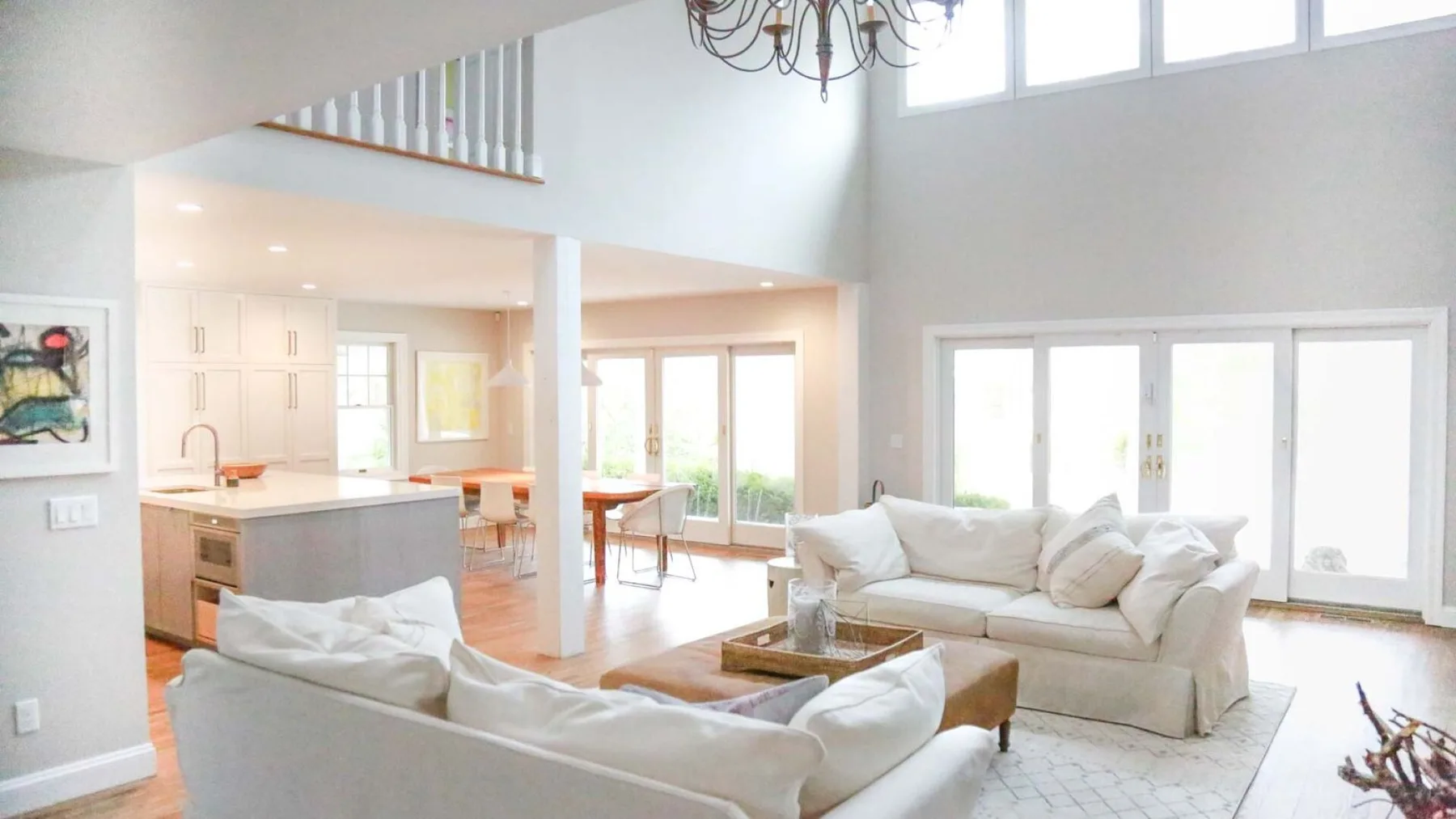 A bright open-plan living room with white seating and a dining area.