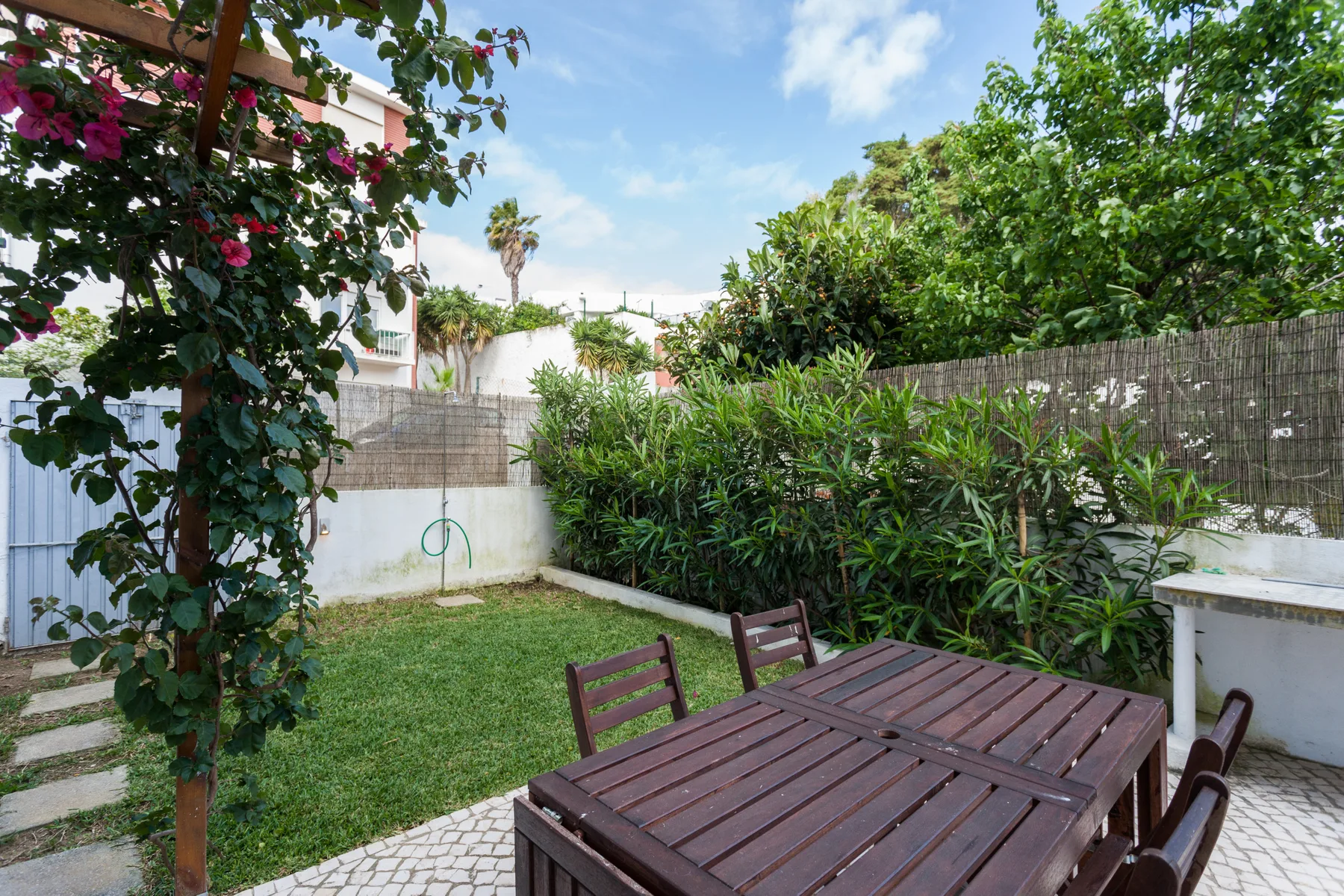 Un patio exterior con una mesa de madera, asientos y un pequeño césped.