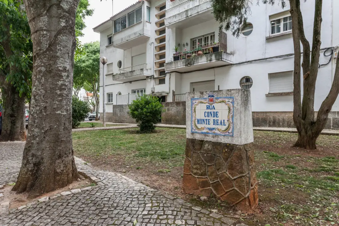 Unos edificios de apartamentos rodean un pequeño patio con árboles y un letrero.