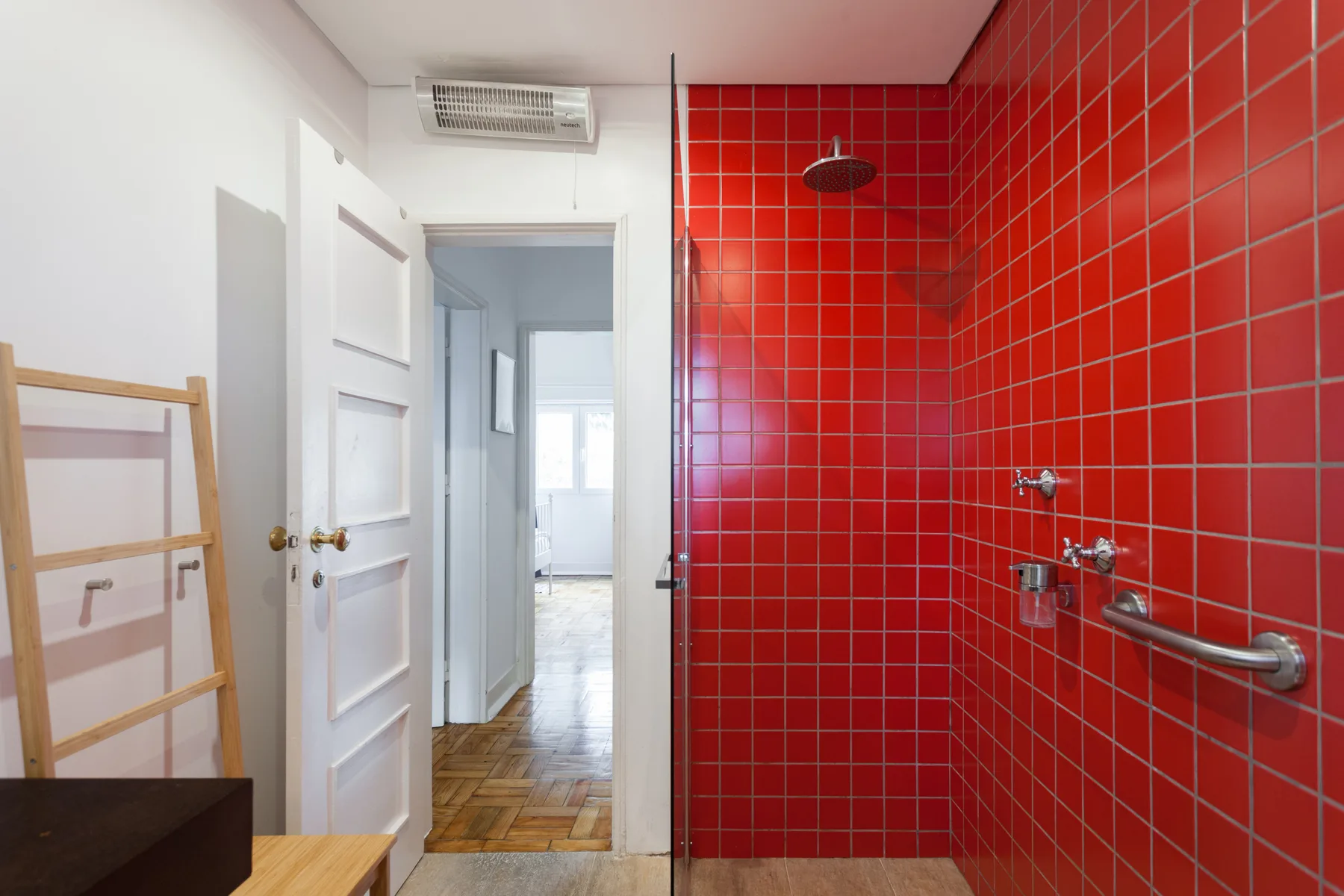 Una zona de ducha con azulejos rojos da a un pasillo luminoso.