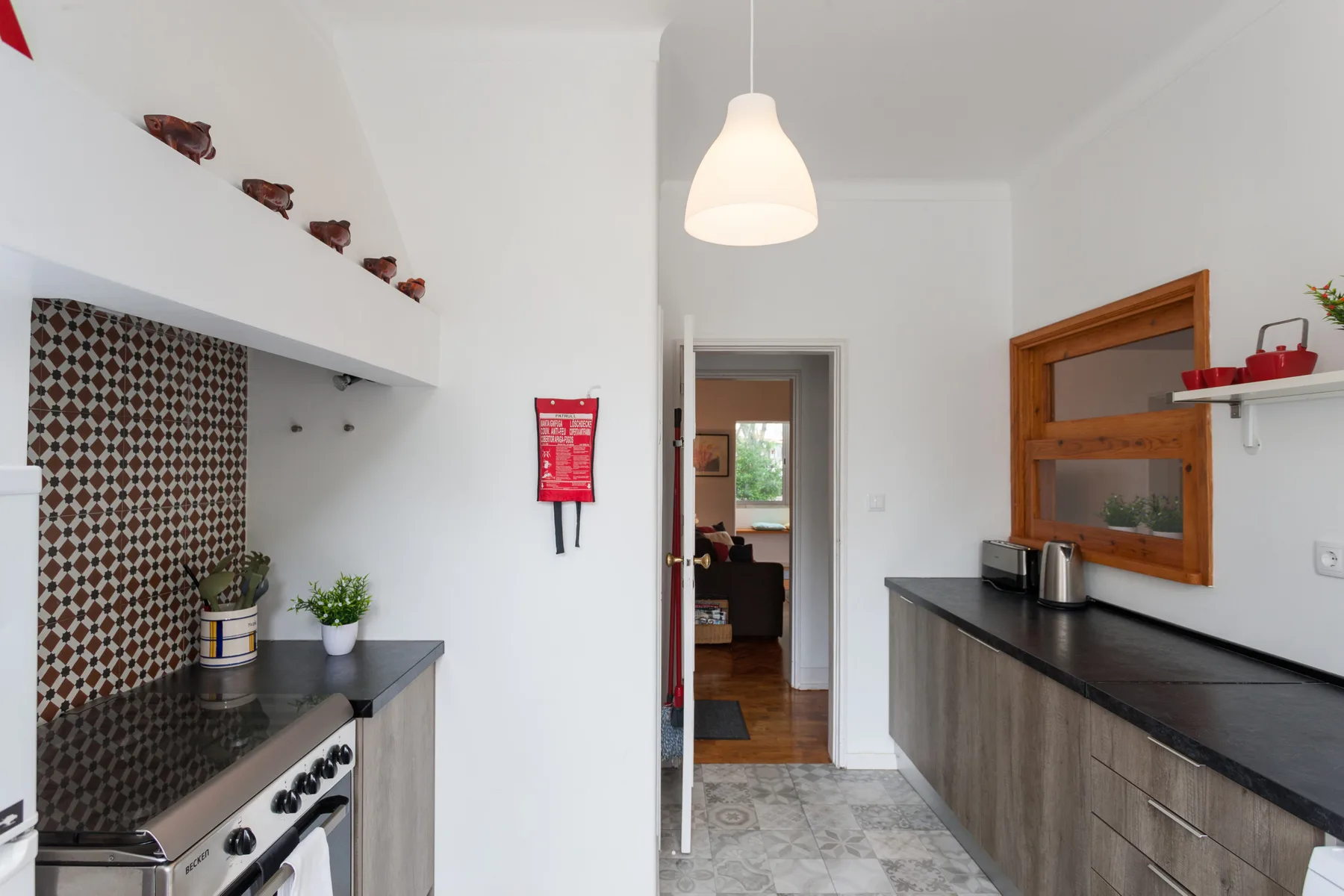Una cocina estrecha con encimeras oscuras y una puerta que da a otra habitación.