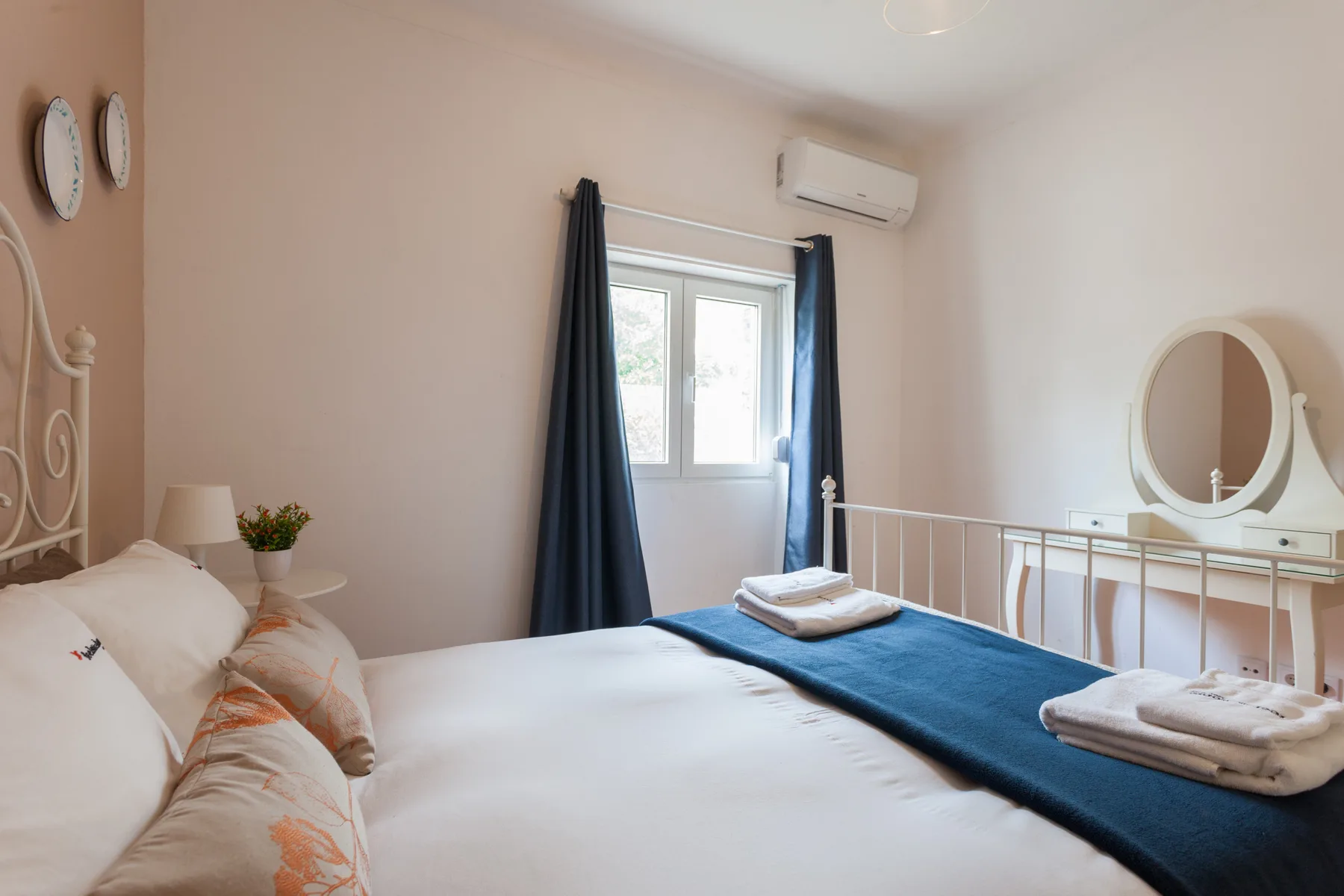 Un dormitorio luminoso con una cama, toallas dobladas y una ventana con cortinas oscuras.