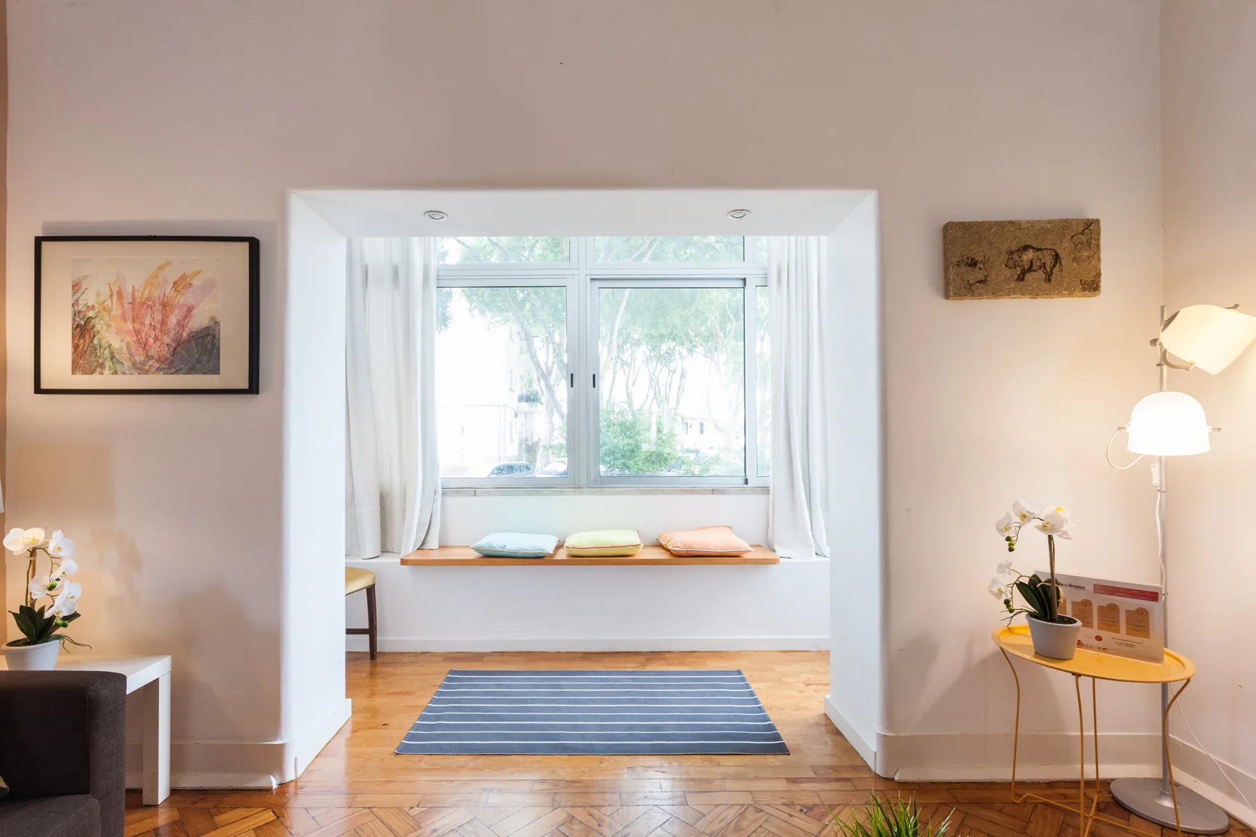 Una sala luminosa con asiento junto a la ventana, alfombra a rayas y lámparas.