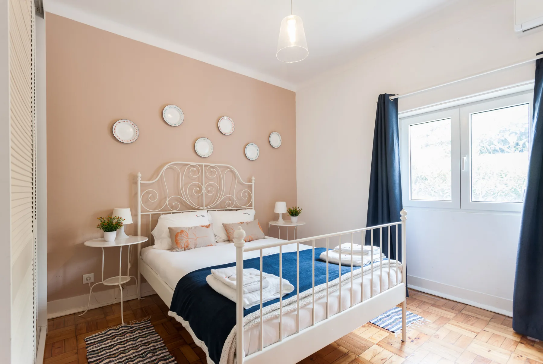 Un dormitorio con una cama blanca, mesitas de noche y una ventana amplia.