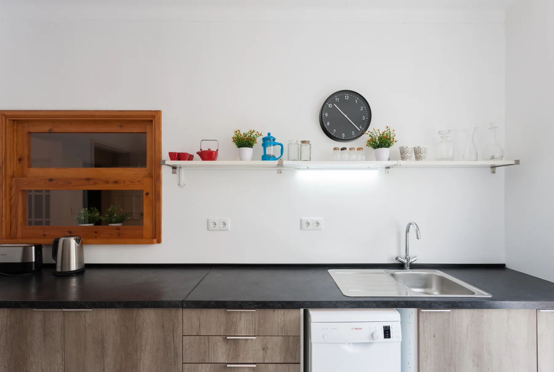 Una cocina moderna con encimera oscura, fregadero y estante de pared.