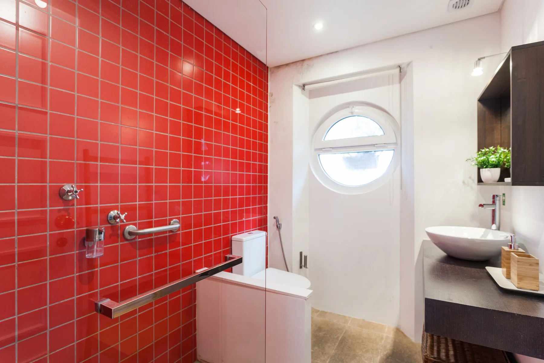 Baño con una pared de ducha de azulejos rojos y un lavabo sobre encimera.