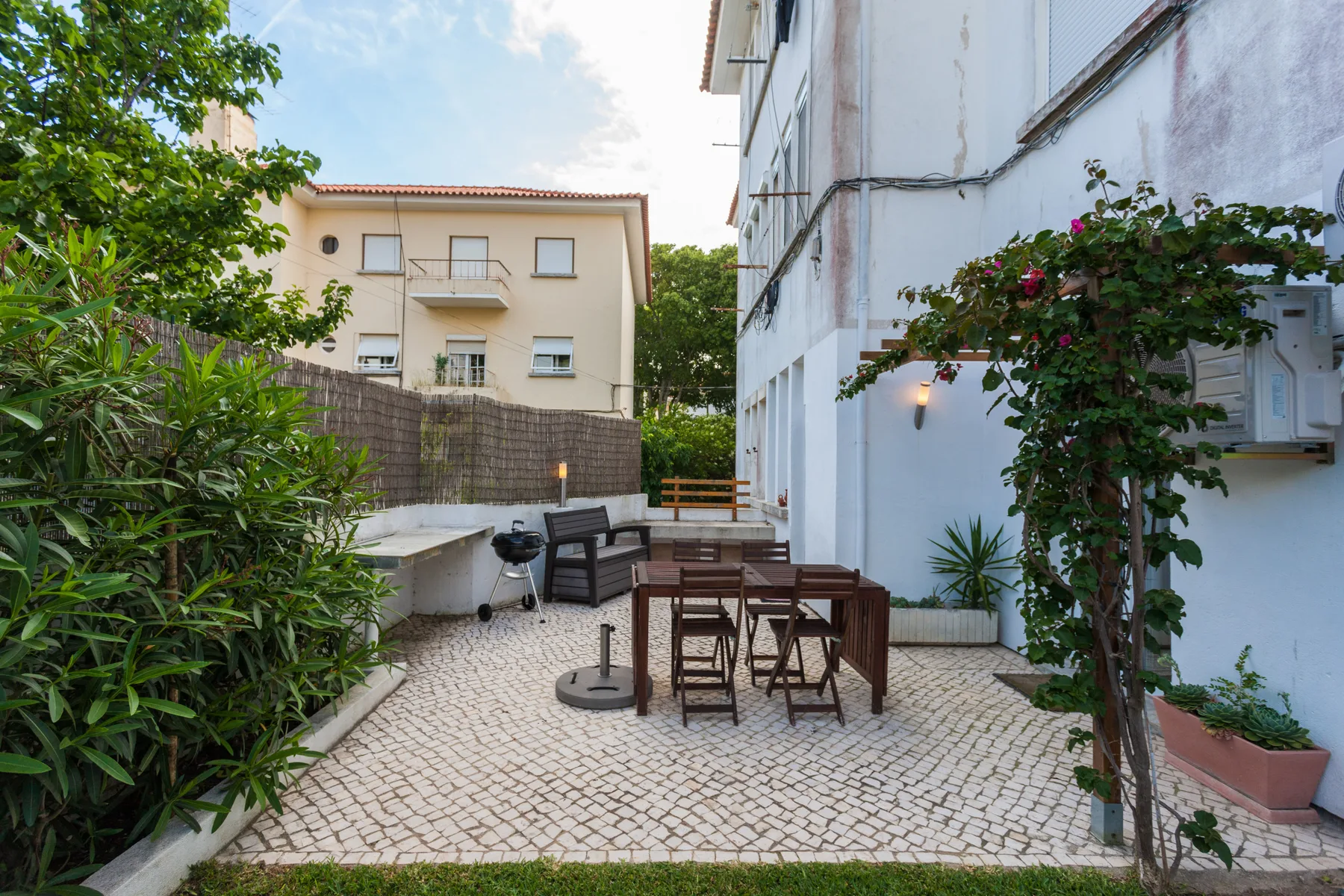 Un patio exterior pavimentado con una mesa de comedor, asientos y plantas alrededor.