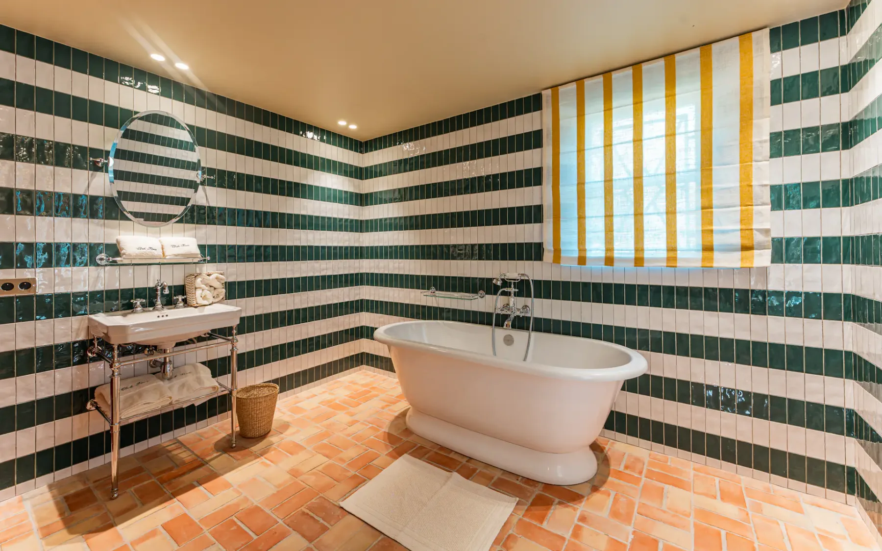 Un baño con una bañera exenta y paredes a rayas verdes y blancas.