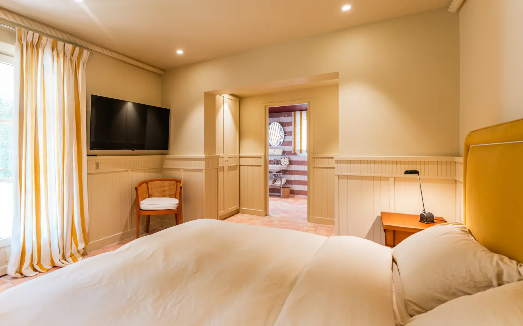 Dormitorio con una cama, televisor en la pared y puerta a otra habitación.