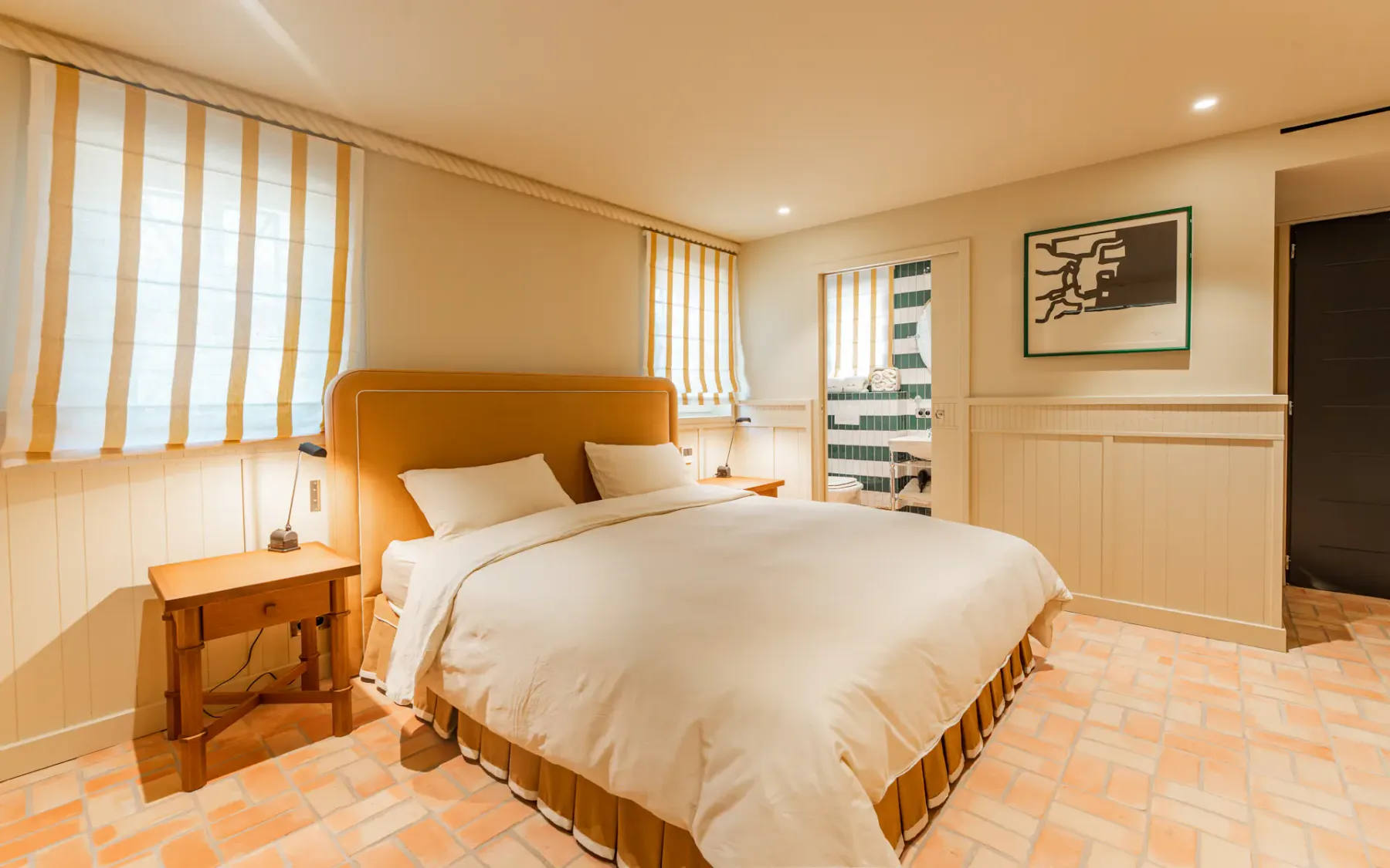 Un dormitorio con una cama doble y una puerta que deja ver un baño alicatado.
