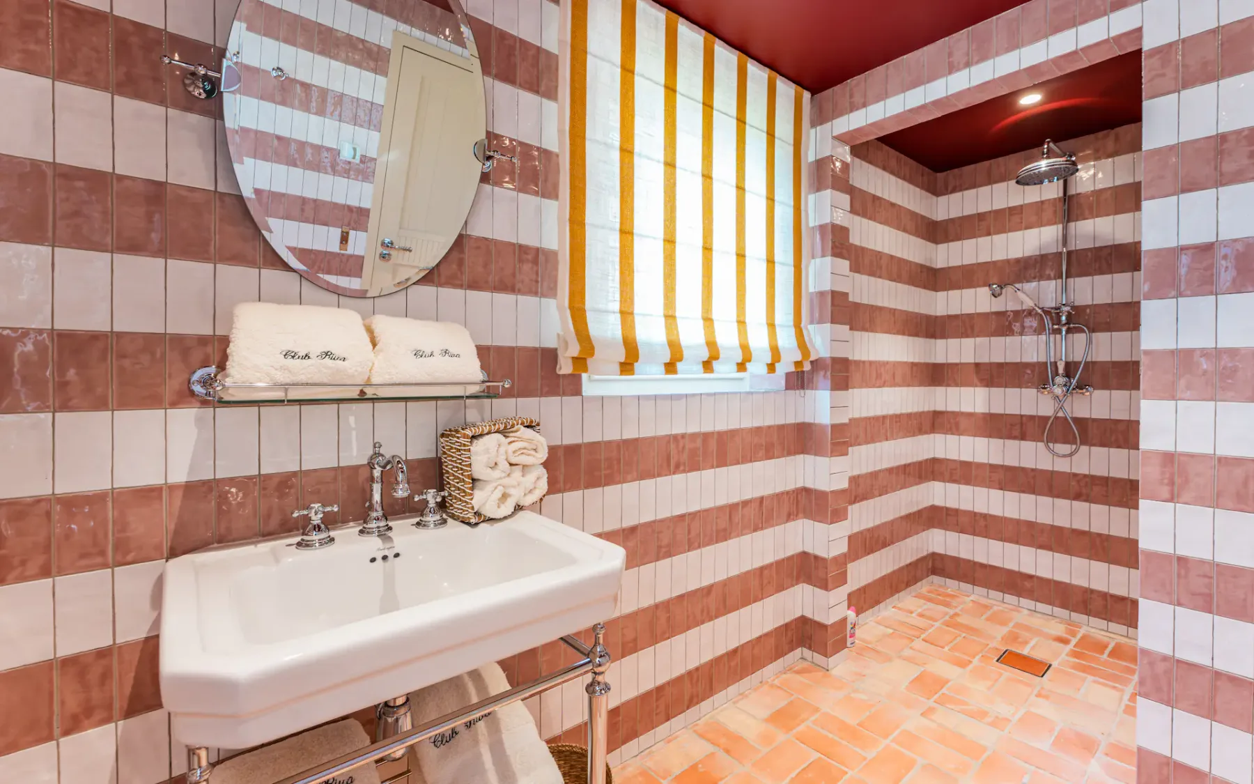 Paredes de azulejos rosas y blancos en un baño con lavabo y espejo y una ducha al fondo