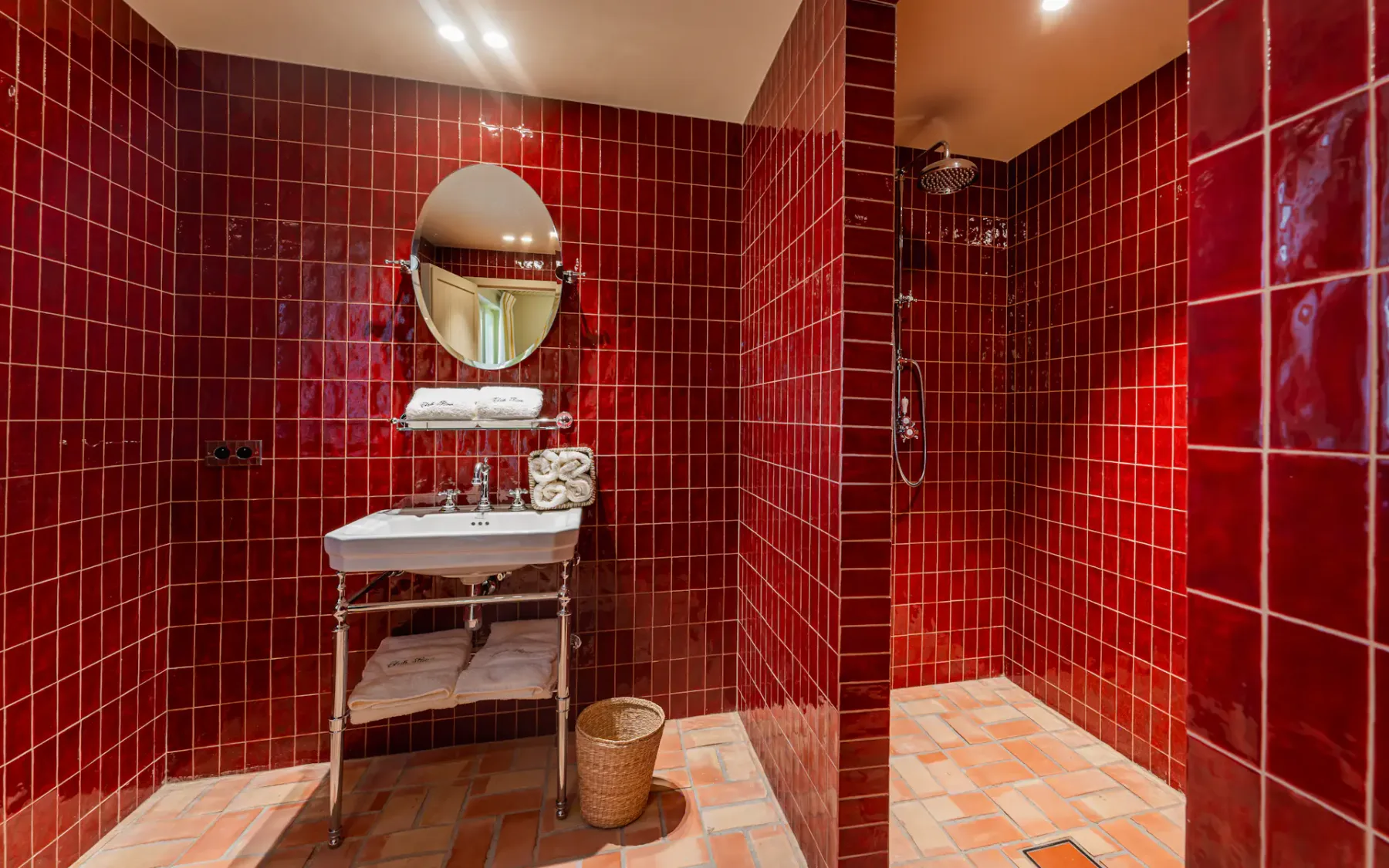 Baño con azulejos rojos, lavabo, espejo y ducha abierta
