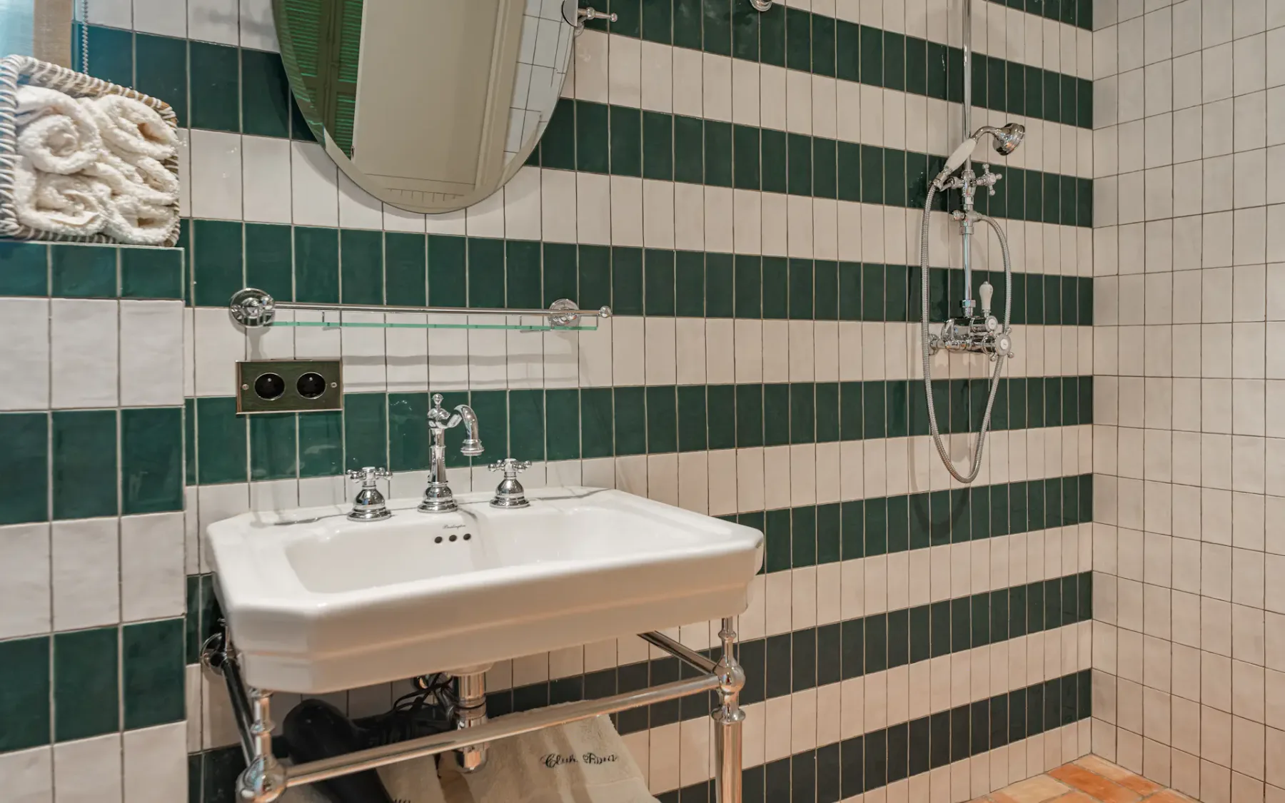 Lavabo y espejo de baño con una pared de azulejos verdes y blancos y una ducha a la derecha