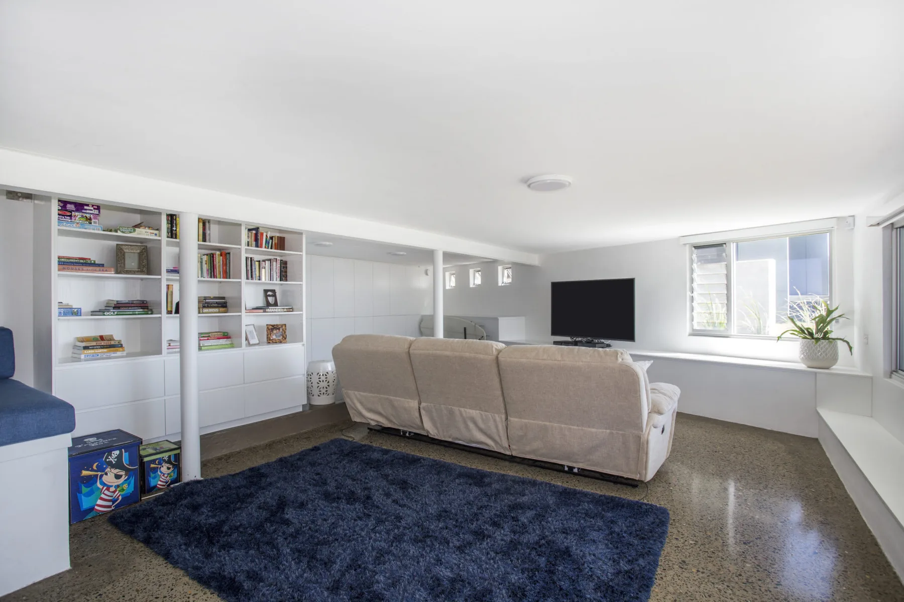 Una sala luminosa con estanterías empotradas, asientos y un televisor.