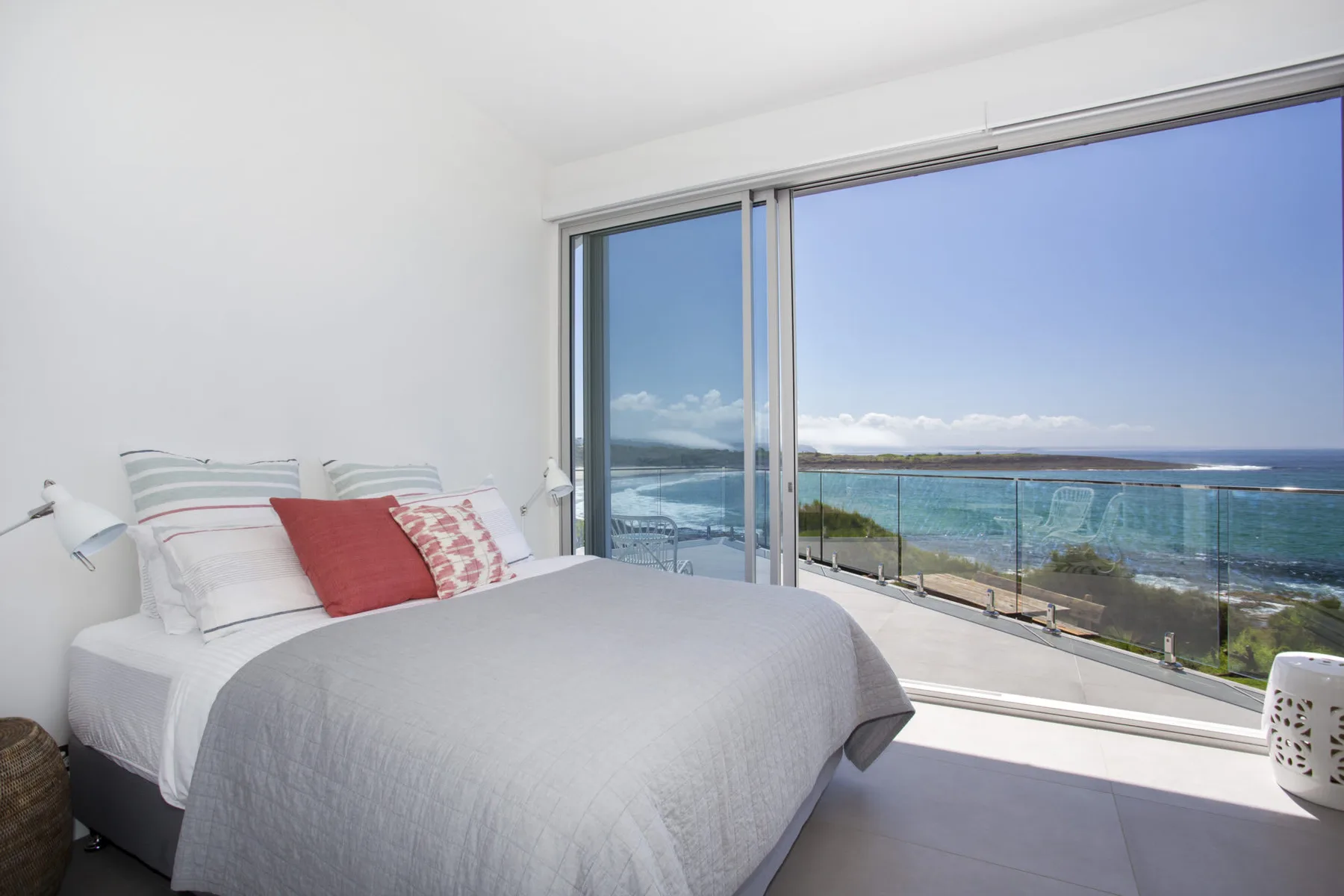 Un dormitorio con una cama junto a grandes ventanales con vista al océano.