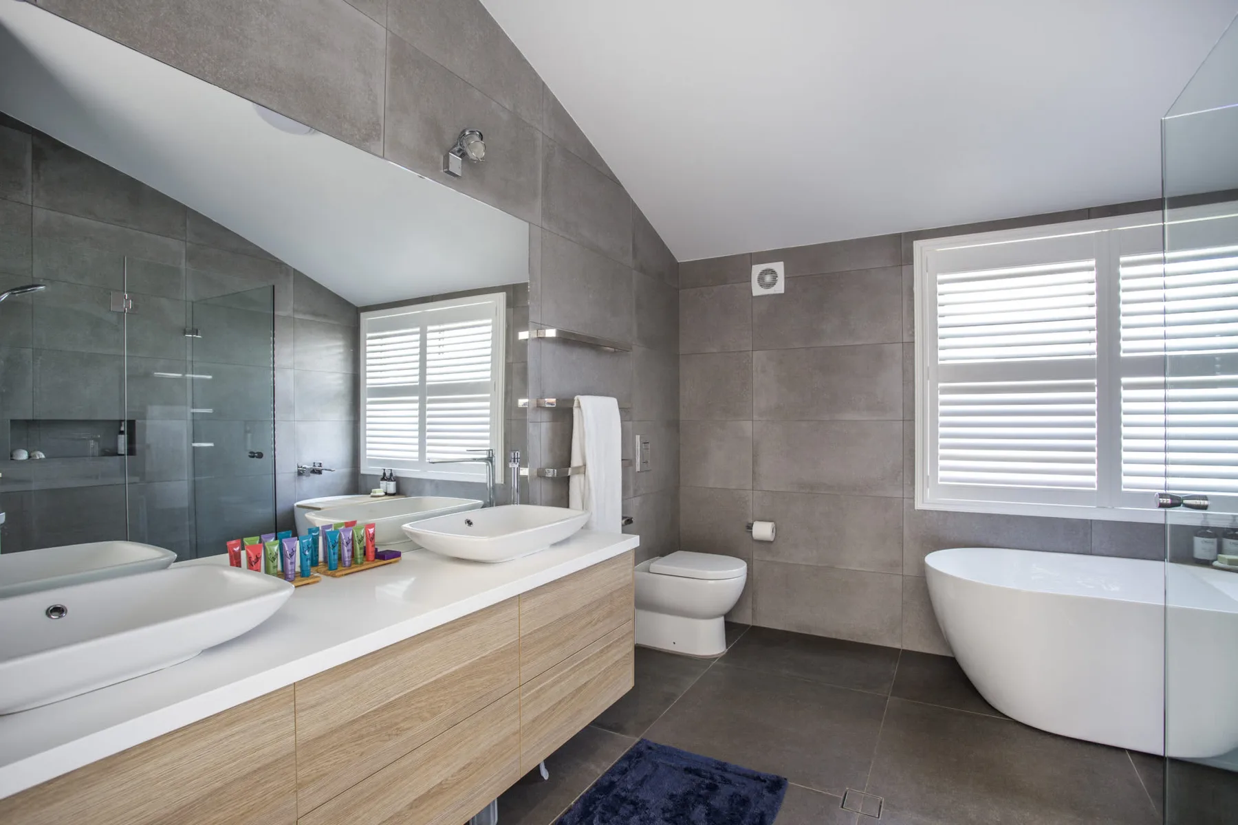 Un baño moderno tiene un tocador con dos lavabos, inodoro y bañera.