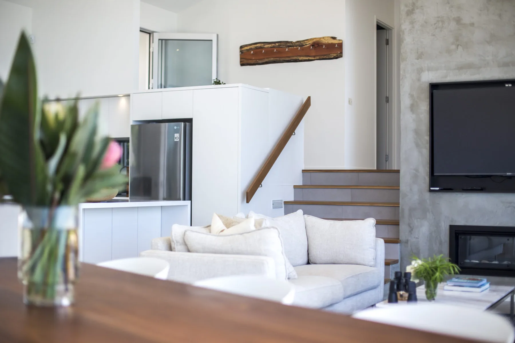Sala de estar con asientos blancos, un televisor y una escalera.