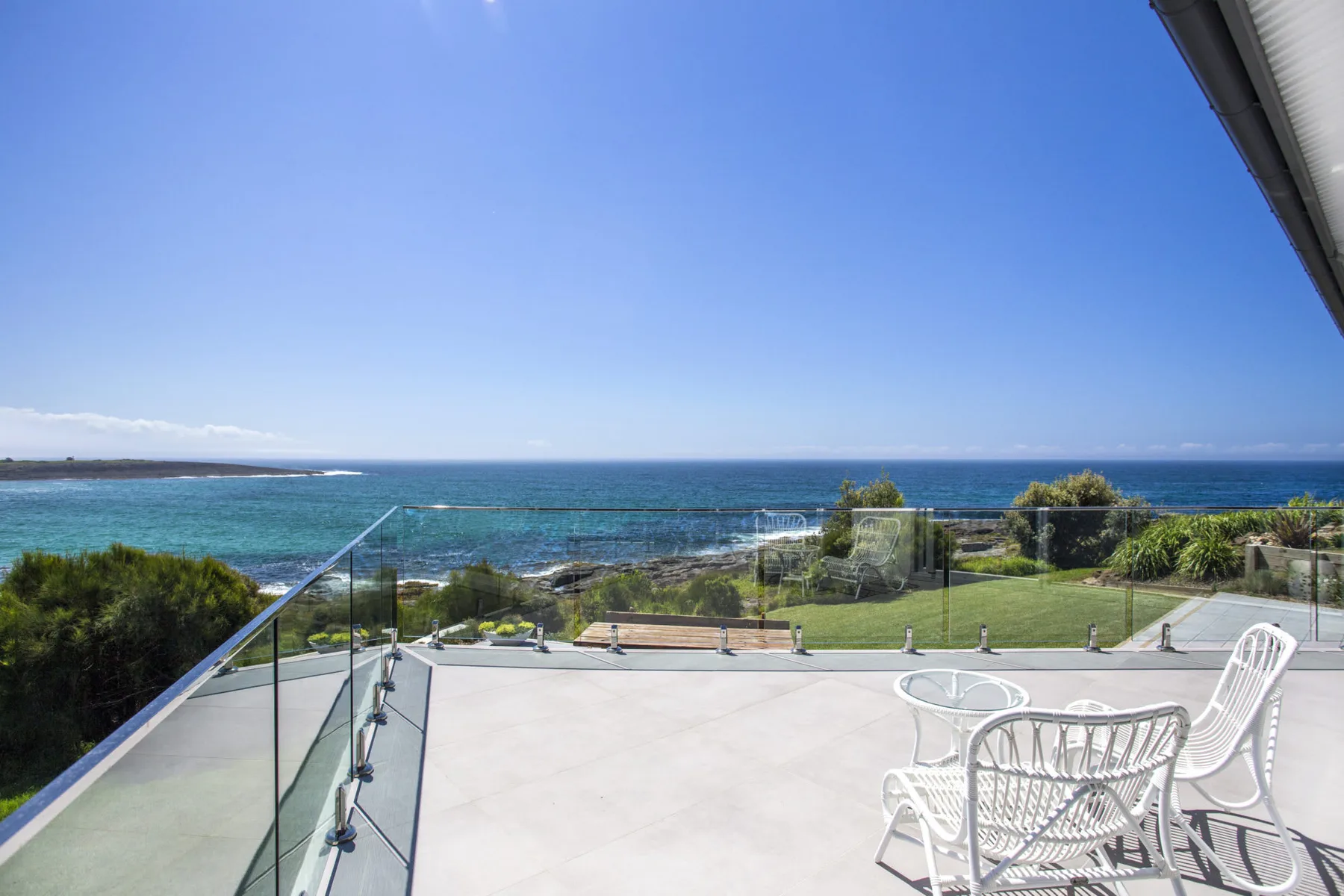 Una terraza junto al mar mira al océano, con asientos al aire libre y una barandilla de vidrio.