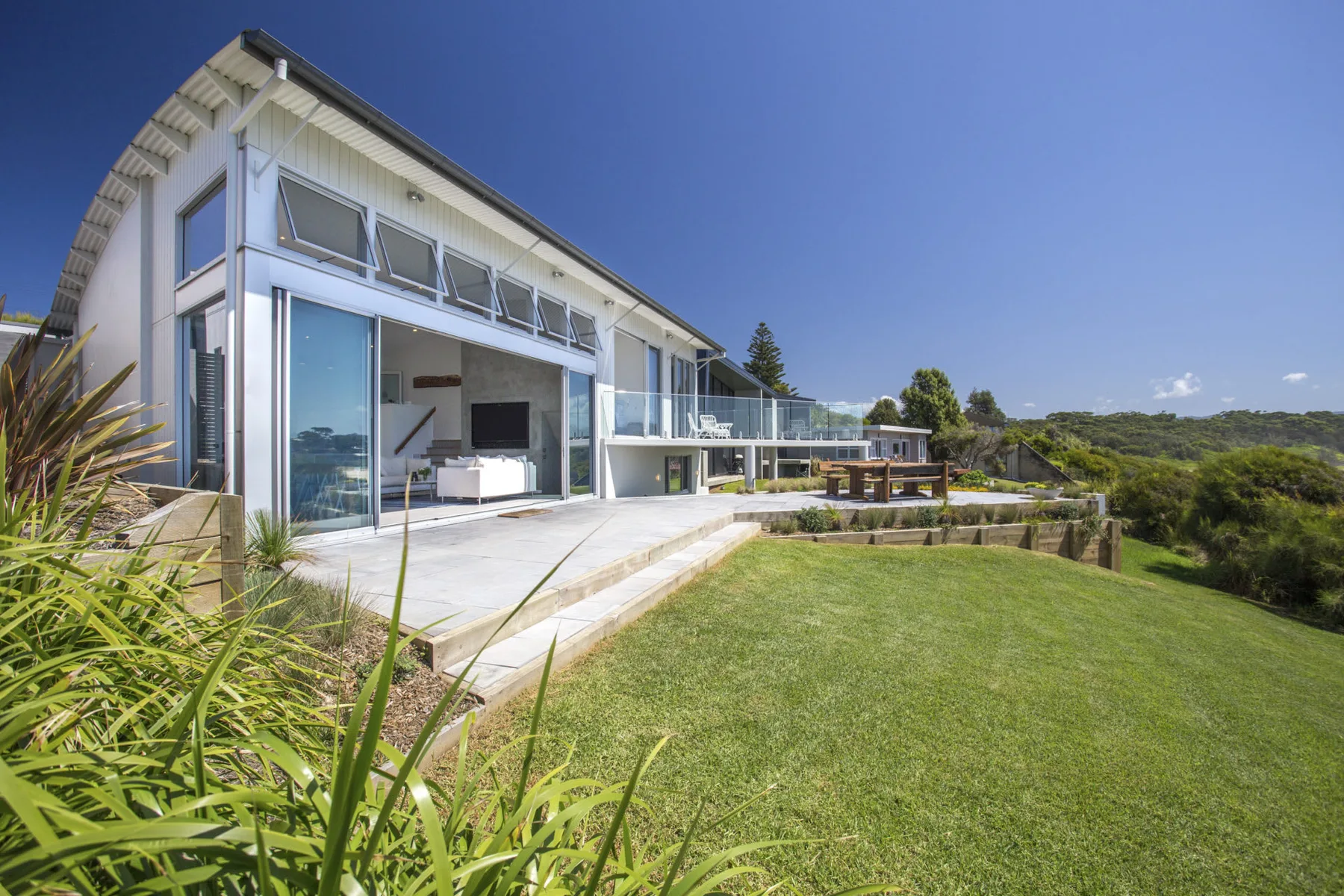 Una casa moderna da a un césped, con una terraza y asientos al aire libre.