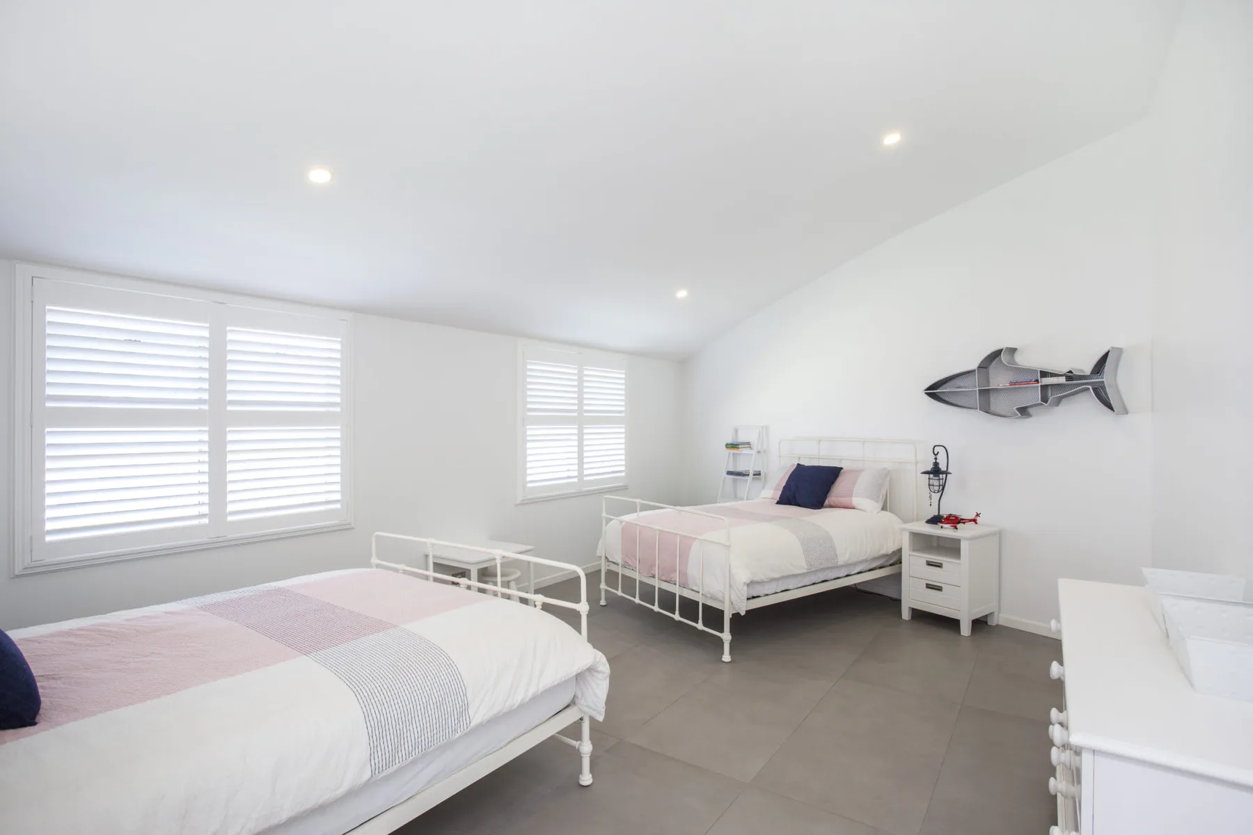 Un dormitorio luminoso con dos camas y ventanas con persianas.