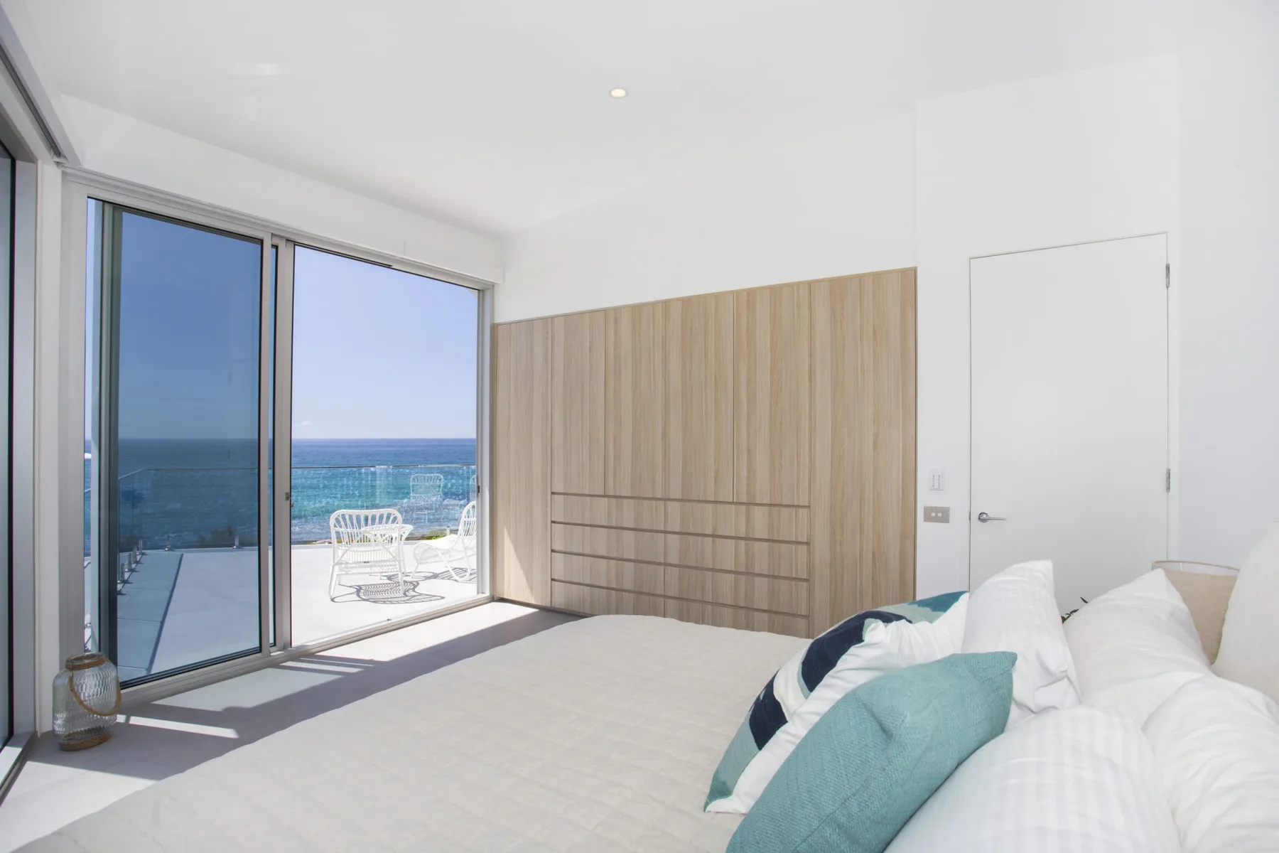 Un dormitorio luminoso con una cama junto a grandes ventanas con vistas al océano.