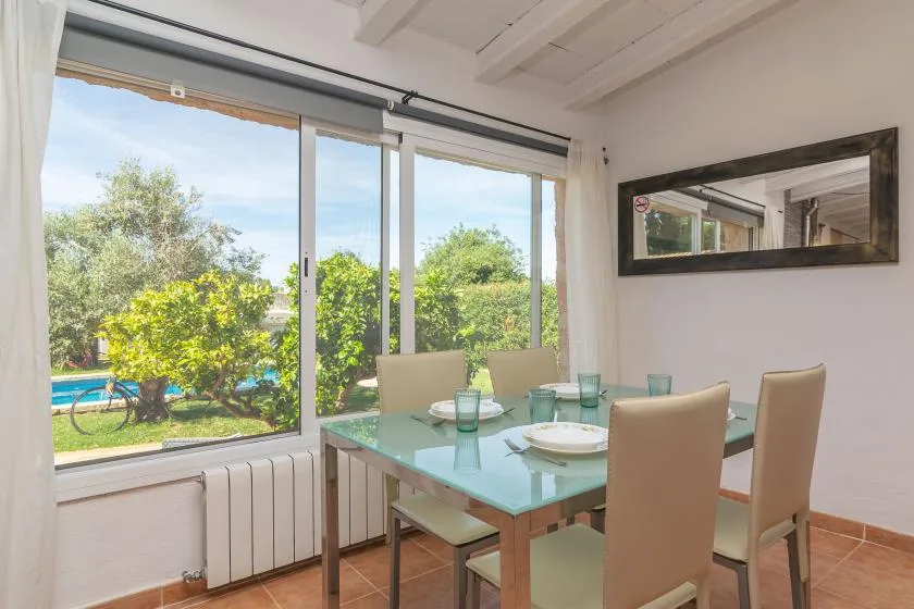 A dining area with a glass table beside large windows overlooking a garden.