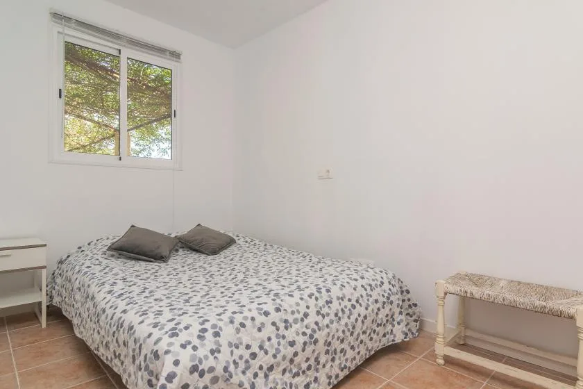 A bedroom with a patterned bed beneath a window overlooking trees.