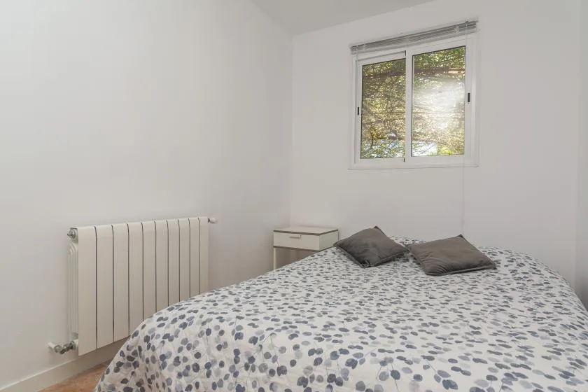 A bedroom with a bed beneath a window and a radiator on the wall.
