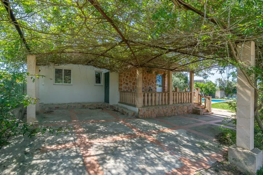 A shaded patio with a stone-faced outdoor seating area and leafy overhead canopy.
