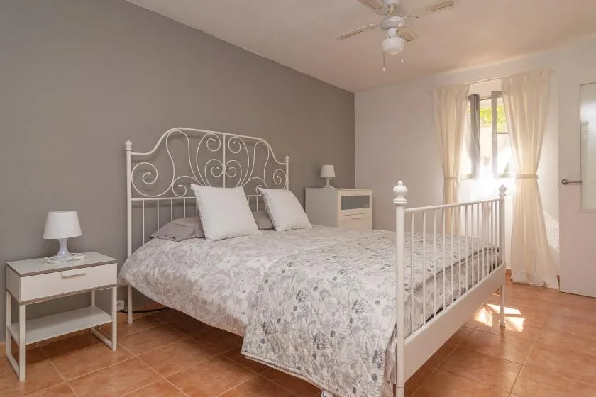 A bedroom with a white metal bed, patterned bedding, and a window with curtains.