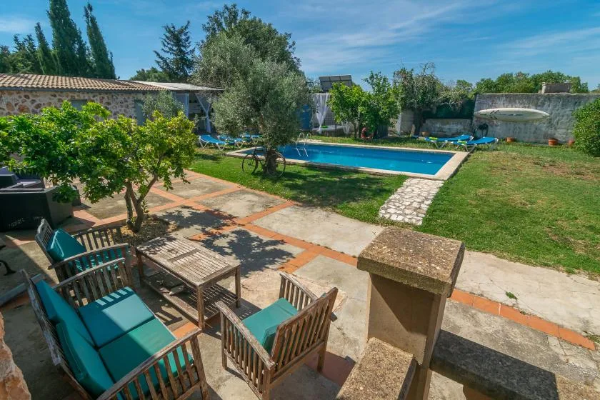 An outdoor pool beside a paved patio with seating and surrounding greenery.