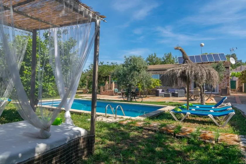 An outdoor swimming pool beside a shaded lounge bed and garden seating.