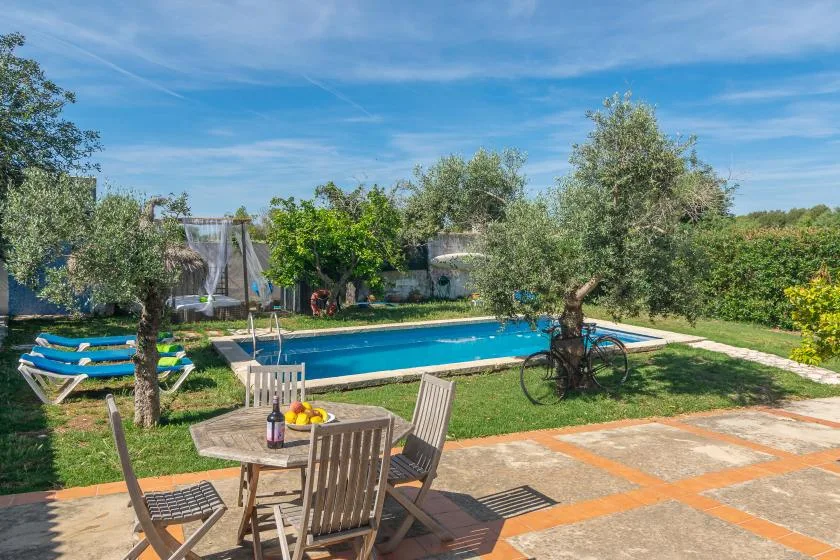 An outdoor swimming pool is surrounded by grass, trees, and patio seating.