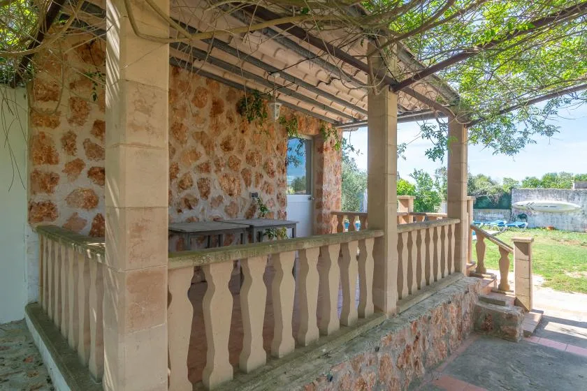 A stone veranda with a balustrade overlooks a green yard.