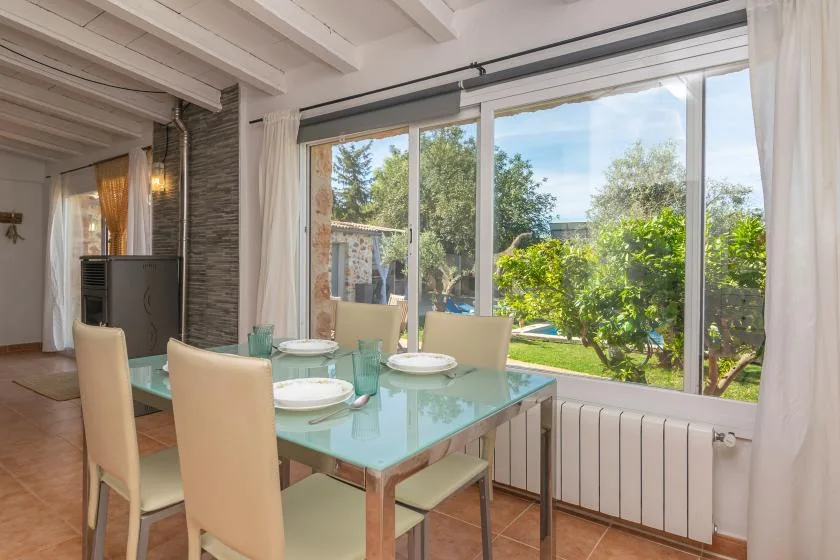 A dining area with a glass table and large windows overlooking a garden.